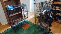 Three black metal shelving units with glass tops arranged in a room on a green carpet with an orange pattern.