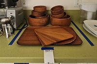 Photo of stacked wood salad bowls and several wood cutting boards laid out on a countertop with a large wood serving tray behind.