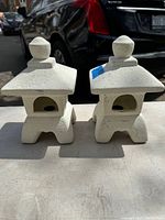 Front view of two stone Asian pagodas with arched opening, displayed outdoors on a flat surface.