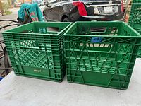 Two green Neilson milk crates on a table, one on the left with diamond pattern sides and one on the right with crossed grid pattern sides.
