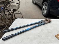 Photo of a 30 inch bolt cutter with blue handles and black grips placed on a white table outdoors, showing signs of wear and rust.