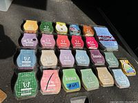 Top down photo showing multiple Scentsy wax melts in clamshell packaging, arranged in rows by color and brand