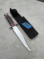 Photo showing fixed blade knife with black and red wrapped handle alongside black fabric sheath.