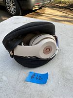 Folded white Beats headphones in black zippered carrying case on outdoor surface