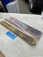 Photo of solid brass incense burner holder with etched patterns and a pack of incense sticks in clear plastic bag on a table.