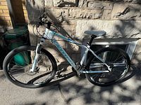 Full side view of white and teal Cannondale hardtail mountain bike leaning against stone wall