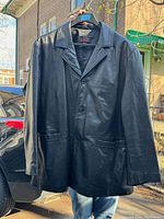 Front view of the Danier men's black leather coat showing button closure, two front pockets, collar, and long sleeves.