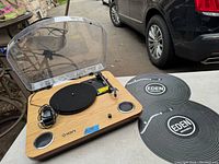 Wood finish ION turntable with clear dust cover, power adapter, and two Eden slipmats placed beside it on a table.