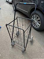 Photo of the large folding shopping cart placed outdoors on pavement, showing front and side views, caster wheels, and handlebar with blue tape.