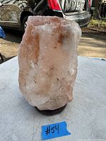 Large rough pink Himalayan salt block on stand, photographed outdoors on table with car tire visible in background.