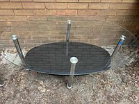 Photo of modern oval coffee table upside down showing beveled clear glass top with chrome legs and black glass lower shelf