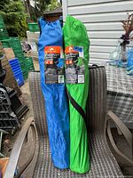 Two deluxe folding camp armchairs in blue and green fabric carrying bags placed on an outdoor chair against a house exterior background.