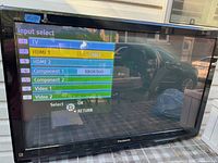 Front view of Panasonic TV showing screen with input select menu and reflections.