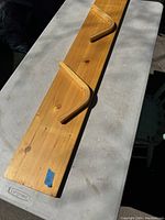 Single pine wood wall shelf with two wooden brackets on a grey surface, showing natural wood grain and knots.