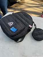 Black Reebok backpack with front pocket and Reebok logo patch, alongside small round zippered black change purse attached with strap and clip.