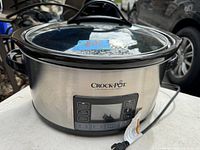 Stainless steel Crock-Pot slow cooker showing front digital control panel and glass lid with black handle.
