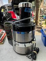 Image showing the front and side angle of the stainless steel and black plastic juicer with chrome safety latch and power cord.