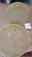 Two sage green metal mesh food covers placed on a surface, showing top and side views with the seller's lot tag visible.