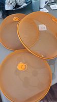 Three large orange mesh food covers on a table, showing mesh detail and handles.