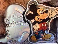 Cake pans shaped like cartoon characters Smurf and Mickey Mouse with detailed embossing in aluminum.