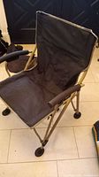 Front angled view of the black foldable camping chair placed indoors on tiled floor showing fabric seat, backrest, armrests and frame.
