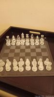 Complete glass chess set arranged on glass chessboard showing both sides, pieces in starting positions.