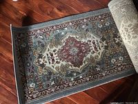 Hallway runner rug partially rolled, showing detailed medallion pattern and border on hardwood floor.
