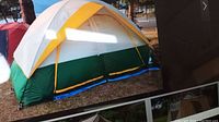 Photo showing assembled dome tent in yellow, green, and white colors outdoors with visible vent windows and fly sheet setup.