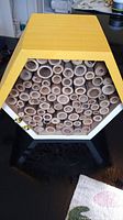 Front view of the hexagonal yellow and white bee house showing multiple hollow tubes for bee nesting.