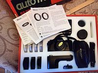 Top view of Pentax Auto 110 camera kit in original box showing camera, multiple lenses, viewfinder, and manuals.