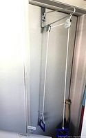 Photo showing shoulder pulley device mounted over the top of a door with metal bracket and rope hanging down.