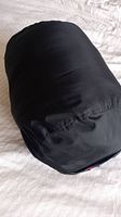 Sleeping bag rolled up in its black outer shell on a light surface, showing no visible damage.