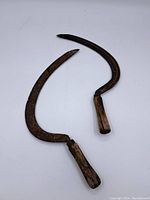 Two antique sickles with curved blades and wooden handles on a flat white background, showing wear and rust consistent with age.