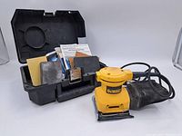 Full lot display showing DeWalt palm sander, carrying case, sanding sheets, manuals, and dust collection bag.