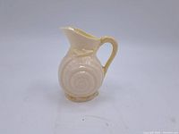 Front view of small vintage milk glass creamer pitcher showing snail shell relief design and flared spout.