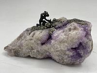 Side view of quartz rock specimen showing purple and white quartz, pyrite deposits, and mounted mining figure in black metal.