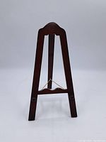 Front view of the wooden art frame stand showing carved top and brass wire support