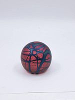 Close-up side view of the spherical paperweight showing the reddish-pink base with dark blue abstract web-like pattern.