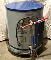 Front view of cylindrical water heater with blue top, pipes with red and blue handles, and electrical cover box.