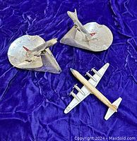 Three vintage airplane desk display models on purple cloth: two Swissair Douglas DC-8 airplane ashtrays with rotating planes and one Tekno Denmark Douglas DC-7 model.