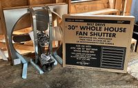 Whole house fan with fan blades, belt drive motor and frame alongside unopened shutter box.