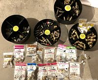 Lot overview showing four black storage bins filled with various brass plumbing fittings plus multiple plastic bags with brass fittings arranged below.