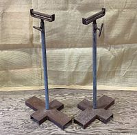 Two cast iron adjustable height outfeed rollers with cross-style bases and horizontal roller tops on a plywood floor, showing the front view.