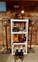 Wide view showing two tall metal lantern-style candle stands, white plastic shelving unit with multiple wooden and ceramic decorative items.