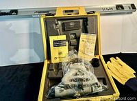 Photo showing the yellow hard plastic case open with a silver metal transit level, Johnson 36" aluminum spirit level atop, yellow gloves on the side, and manuals included in the case