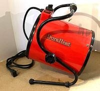 Side and angled view showing red cylindrical powder-coated steel heater body with DuraHeat logo, attached black pivoting metal frame base, power cord, and control knob.