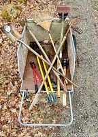 Overhead view inside the garden cart showing various garden tools including rakes, loppers, shovel, and hoe arranged inside the cart.