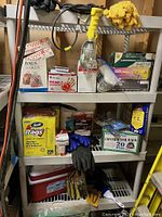 Shelf full of assorted gloves, bags, hand warmers, cleaning products, and a work light