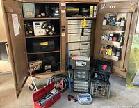 Cabinet doors open showing left shelving and right drawers, assorted tools and boxes arranged inside and in front.