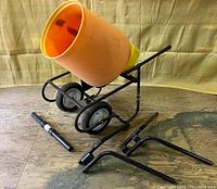 Orange polyethylene drum mounted on black wheeled steel frame with two polyurethane wheels, with disassembled frame and stand pieces displayed